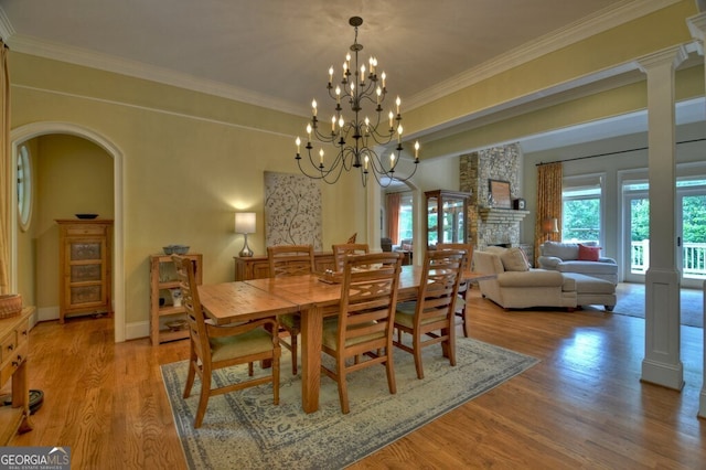 dining room featuring light wood-style floors, crown molding, a stone fireplace, and a chandelier