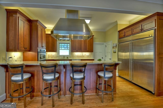 kitchen with island exhaust hood, light wood finished floors, appliances with stainless steel finishes, and light stone counters