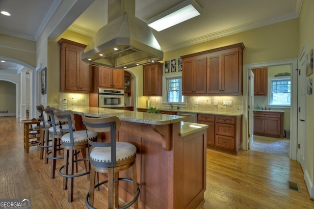 kitchen featuring arched walkways, stainless steel appliances, island exhaust hood, visible vents, and ornamental molding