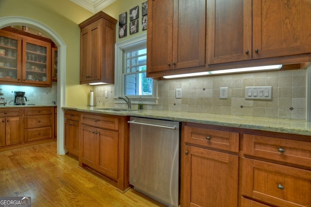 kitchen with brown cabinetry, tasteful backsplash, stainless steel dishwasher, a sink, and light wood finished floors