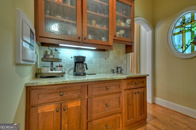 bar featuring a sink, light wood finished floors, arched walkways, baseboards, and backsplash