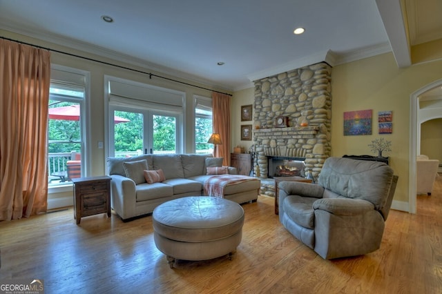 living room featuring crown molding, light wood-style floors, a stone fireplace, recessed lighting, and arched walkways