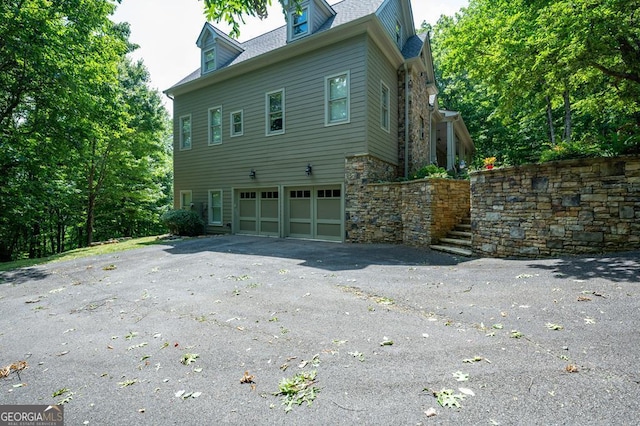 view of side of home featuring driveway, stairs, stone siding, and a garage