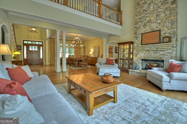 living area featuring an inviting chandelier, a high ceiling, wood finished floors, and a stone fireplace