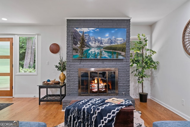 living room featuring wood finished floors, baseboards, and a brick fireplace