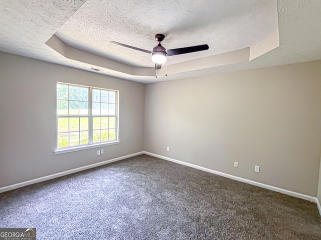 spare room with ceiling fan, a textured ceiling, baseboards, a tray ceiling, and dark carpet