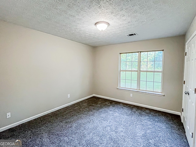 empty room with a textured ceiling, baseboards, visible vents, and dark carpet