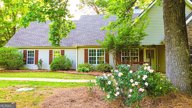 view of front of home featuring a porch, a shingled roof, a front lawn, and a chimney
