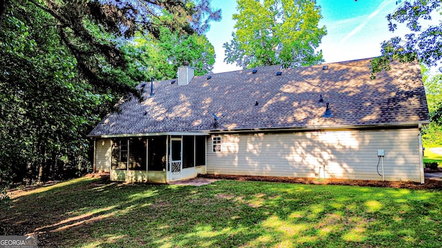 back of house featuring a sunroom, a shingled roof, a lawn, and a chimney