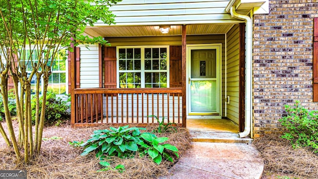 doorway to property with a porch and brick siding