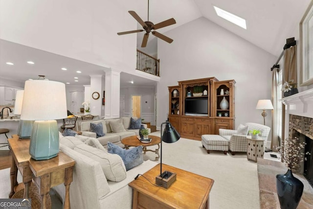 carpeted living area with ceiling fan, a skylight, a fireplace, high vaulted ceiling, and recessed lighting