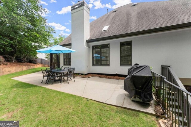 back of house with a chimney, roof with shingles, a lawn, fence, and a patio