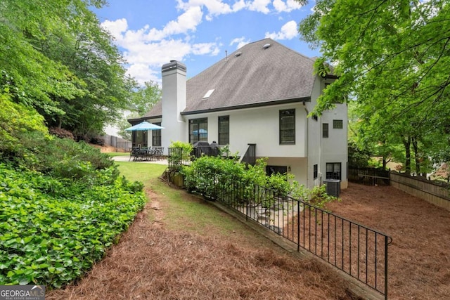 rear view of house featuring a chimney, a patio area, a fenced backyard, a shingled roof, and stucco siding