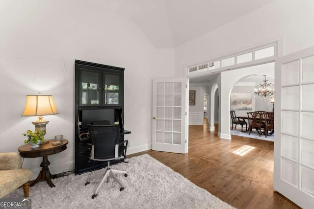 office space with french doors, arched walkways, wood finished floors, high vaulted ceiling, and an inviting chandelier