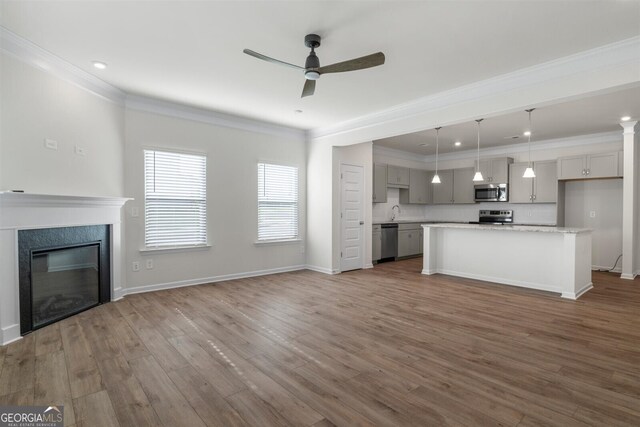 unfurnished living room with crown molding, wood finished floors, baseboards, a high end fireplace, and a ceiling fan