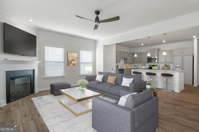 living room featuring ceiling fan, a high end fireplace, wood finished floors, baseboards, and ornamental molding