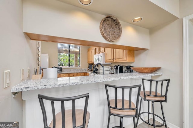 kitchen with light stone countertops, a sink, light brown cabinets, a breakfast bar area, and a peninsula