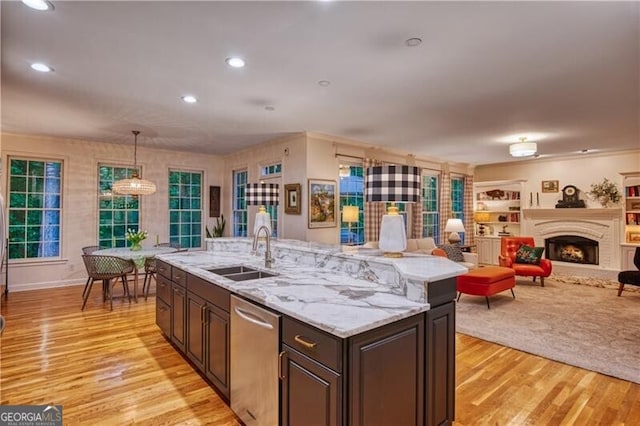 kitchen featuring a sink, stainless steel dishwasher, open floor plan, light wood-style floors, and hanging light fixtures
