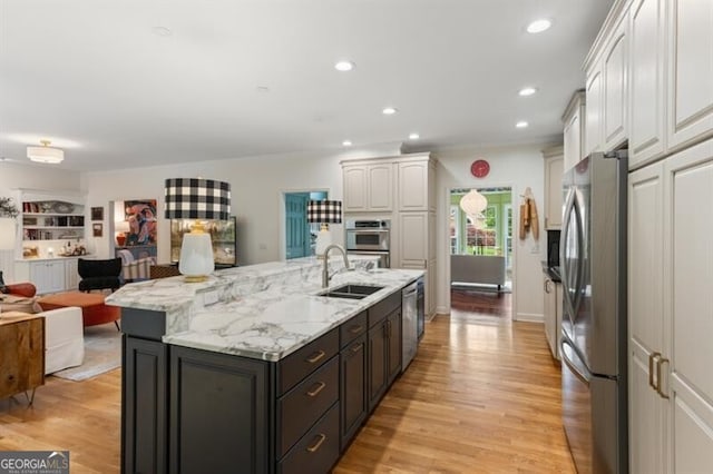 kitchen with appliances with stainless steel finishes, a sink, open floor plan, a center island with sink, and light wood-style floors