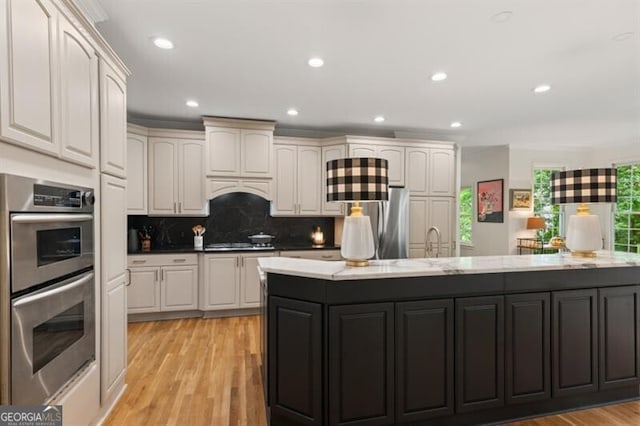 kitchen featuring appliances with stainless steel finishes, light wood-style flooring, decorative backsplash, recessed lighting, and a large island
