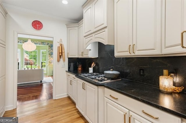 kitchen with light wood-style flooring, stainless steel gas cooktop, crown molding, tasteful backsplash, and white cabinets