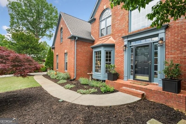 property entrance featuring brick siding and a shingled roof
