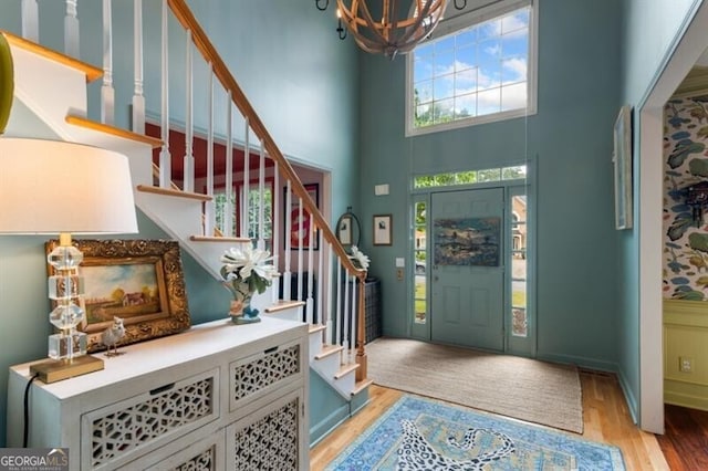 foyer entrance featuring a towering ceiling, a chandelier, light wood-style floors, and stairway