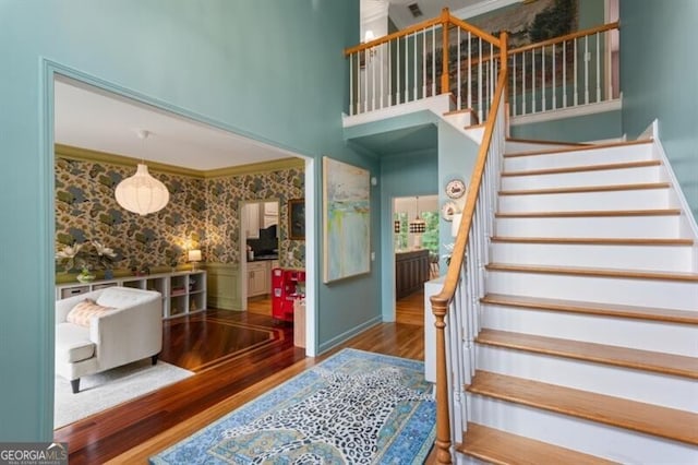staircase featuring wood finished floors, wallpapered walls, and a towering ceiling