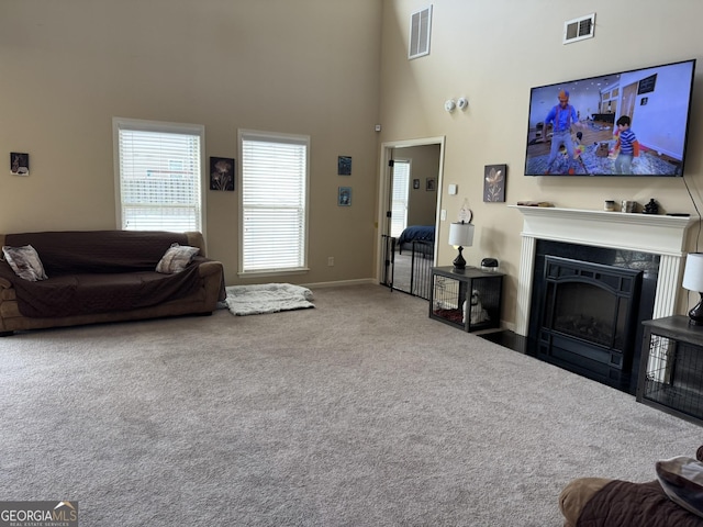 carpeted living room featuring a towering ceiling, baseboards, a fireplace, and visible vents