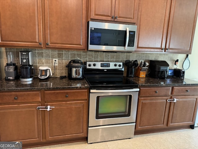 kitchen with brown cabinets, backsplash, stainless steel appliances, and dark stone countertops