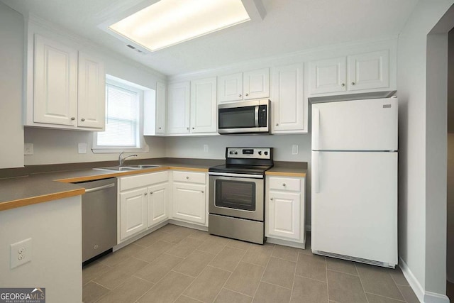 kitchen with a sink, dark countertops, stainless steel appliances, and white cabinetry