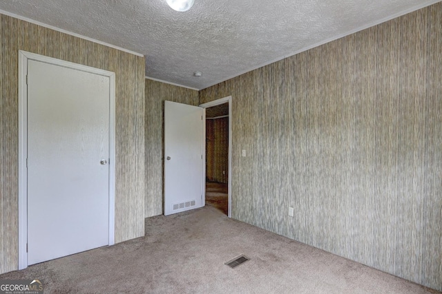 unfurnished bedroom featuring ornamental molding, carpet flooring, a textured ceiling, and visible vents