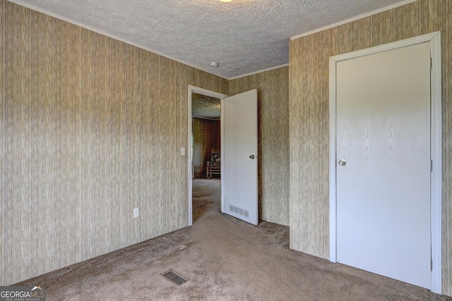 unfurnished bedroom featuring visible vents, ornamental molding, carpet, and a textured ceiling