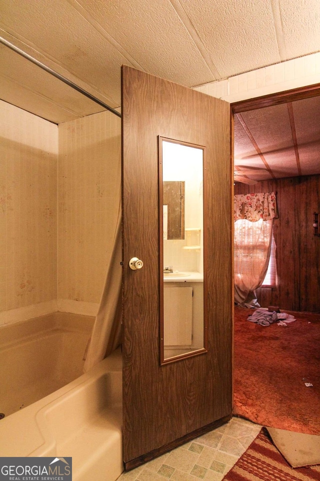 bathroom featuring wood walls, a sink, and shower / tub combo with curtain