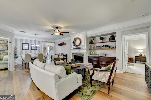 living area with light wood finished floors, a fireplace, ceiling fan with notable chandelier, visible vents, and ornamental molding