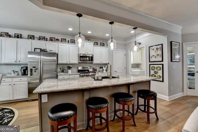 kitchen with white cabinets, appliances with stainless steel finishes, a sink, separate washer and dryer, and backsplash