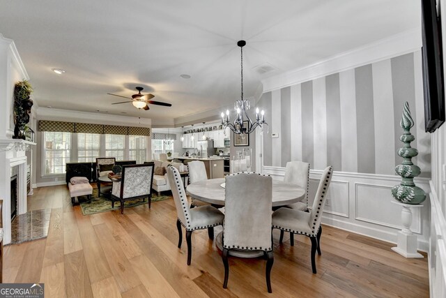 dining room featuring a fireplace with flush hearth, ornamental molding, light wood finished floors, and ceiling fan with notable chandelier