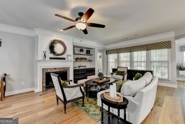 living room featuring ceiling fan, light wood-style floors, baseboards, a high end fireplace, and ornamental molding
