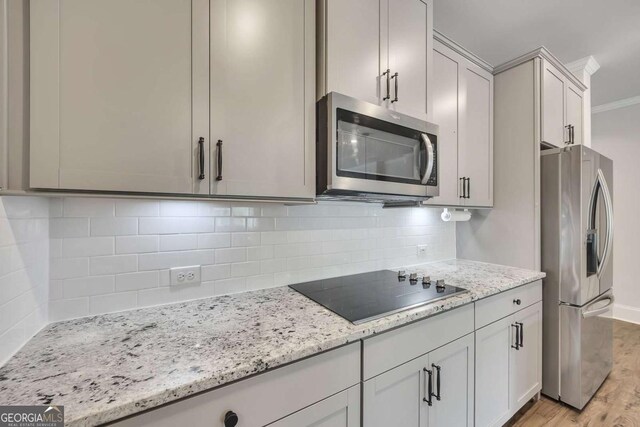 kitchen with crown molding, light stone counters, light wood finished floors, stainless steel appliances, and backsplash