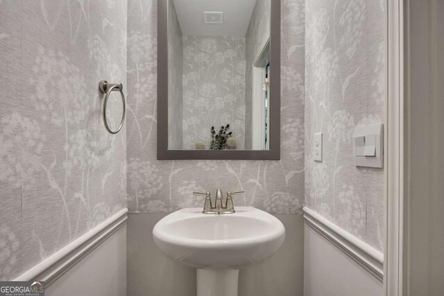 half bath with visible vents, a sink, and wallpapered walls