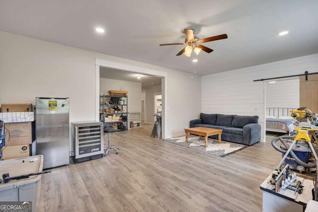 living area with ceiling fan, a barn door, wood finished floors, and wine cooler