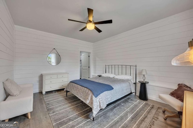 bedroom featuring wooden walls, ceiling fan, and wood finished floors