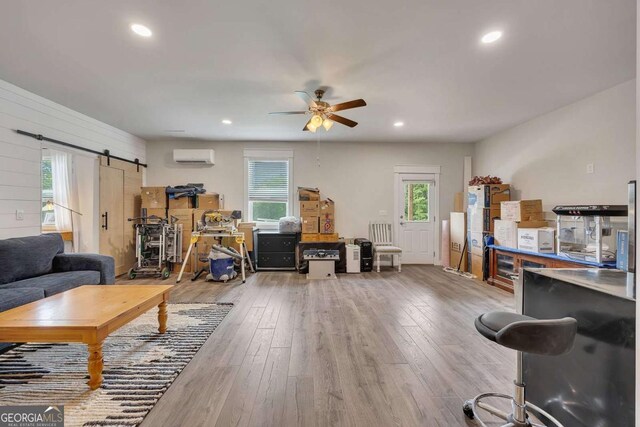living area with a healthy amount of sunlight, a wall mounted AC, wood-type flooring, and a barn door