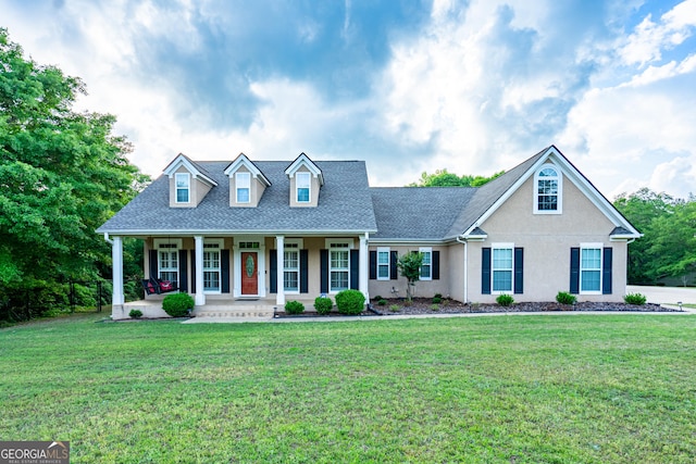 new england style home with a shingled roof, covered porch, stucco siding, and a front yard