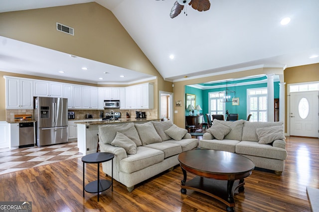 living area featuring high vaulted ceiling, ceiling fan with notable chandelier, recessed lighting, decorative columns, and visible vents