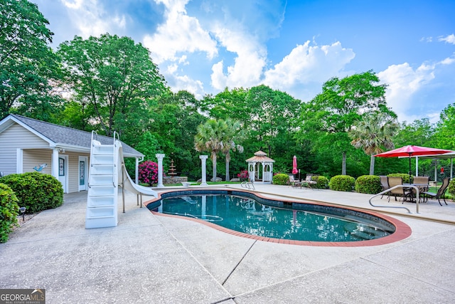 pool with a storage structure, a patio area, a water slide, and an outbuilding