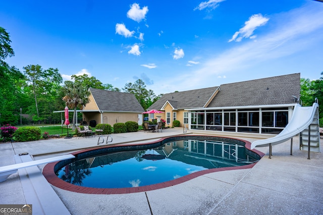 outdoor pool with a patio, a water slide, a sunroom, and a diving board