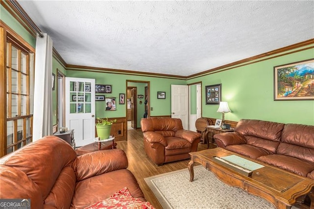 living area with crown molding, a textured ceiling, wood finished floors, and a wainscoted wall