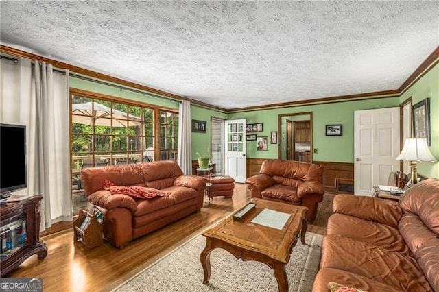 living area with wainscoting, a textured ceiling, ornamental molding, and wood finished floors