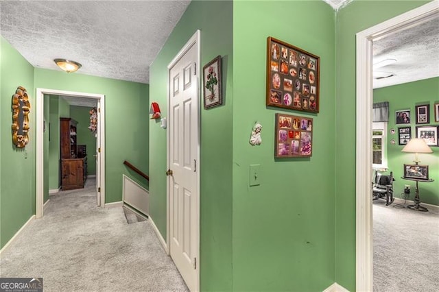 hall featuring baseboards, carpet flooring, a textured ceiling, and an upstairs landing
